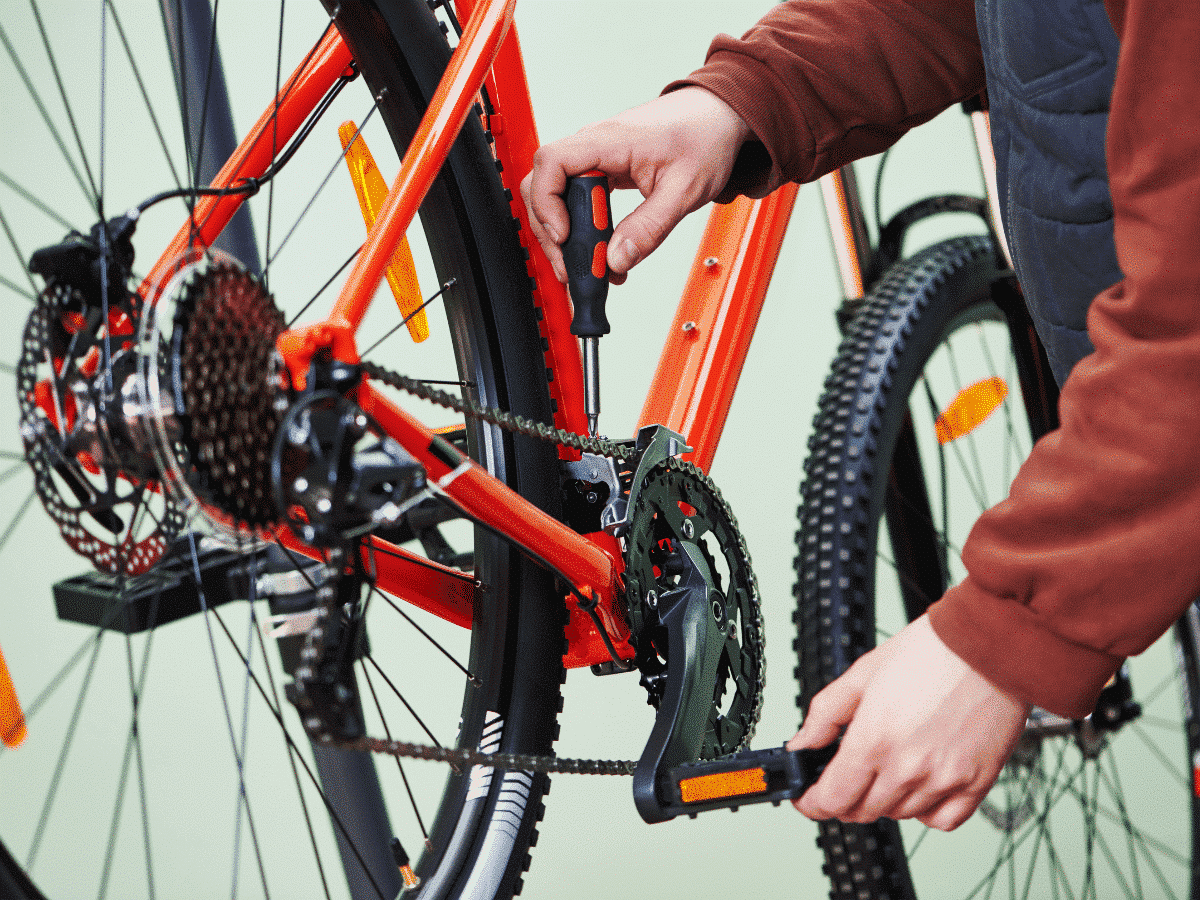 Comment prendre soin de sa chaîne de vélo ? 1 Zoom sur le pédalier d'un vélo. Des mains d'homme font tourner la manivelle et réparent la chaîne.